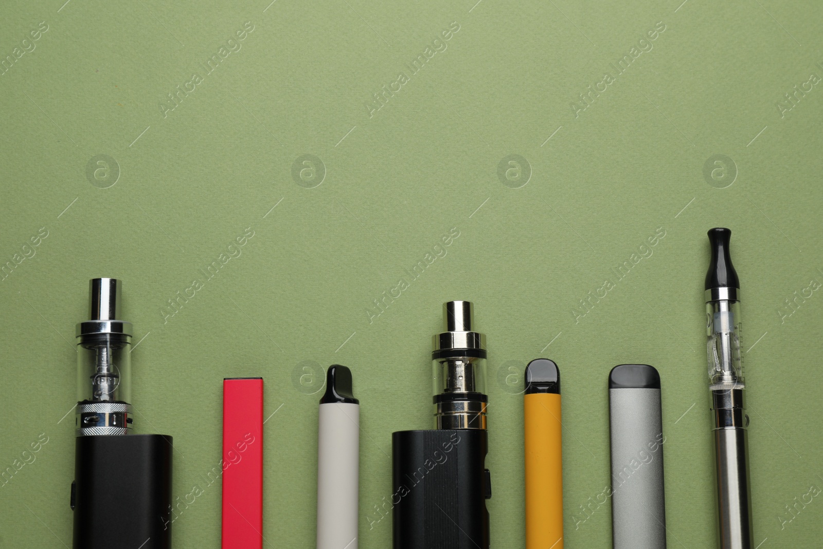 Photo of Many electronic smoking devices on olive background, flat lay. Space for text
