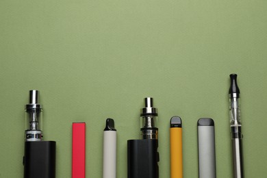 Photo of Many electronic smoking devices on olive background, flat lay. Space for text