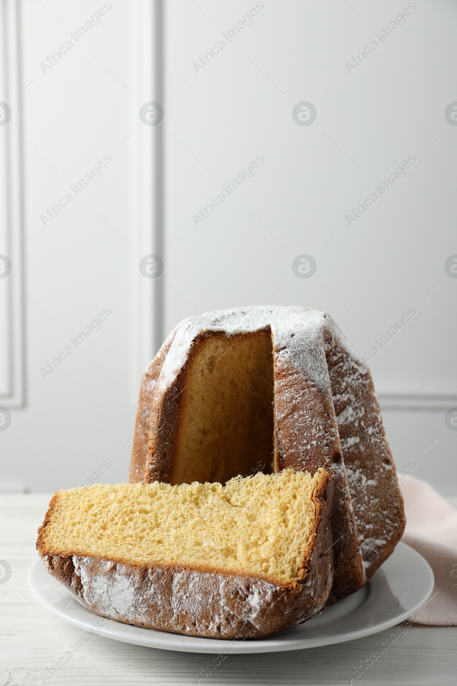 Photo of Delicious Pandoro cake decorated with powdered sugar on white wooden table. Traditional Italian pastry