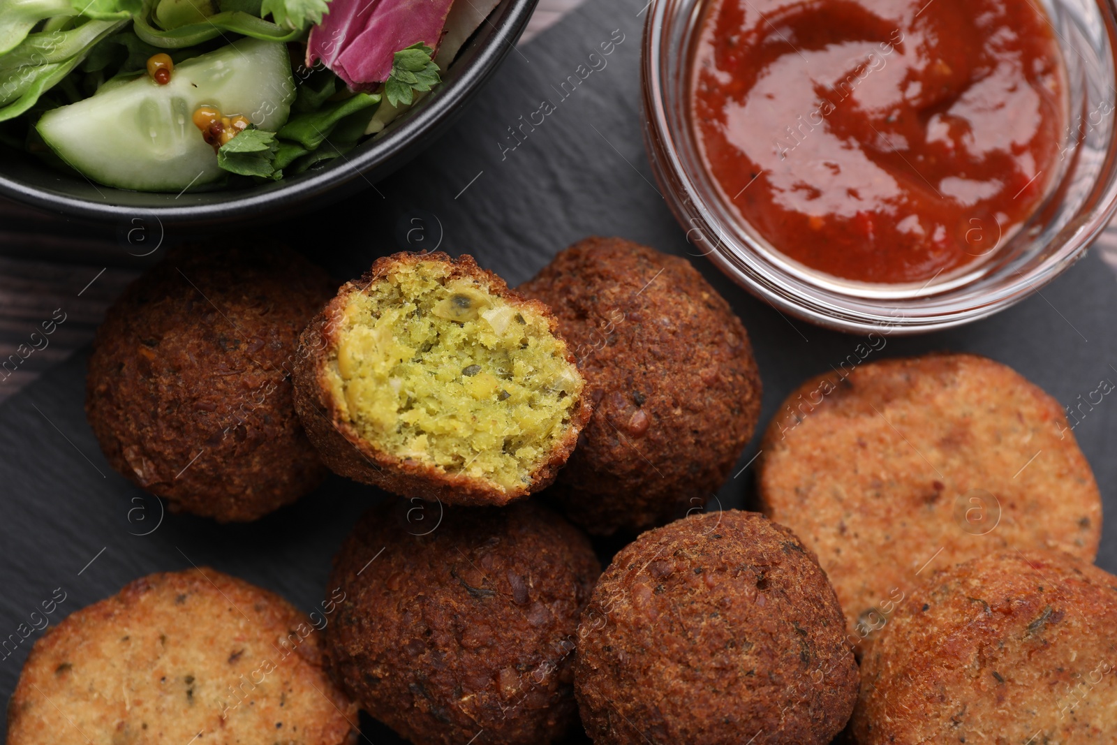 Photo of Delicious vegan cutlets, falafel balls and sauce on slate board, flat lay