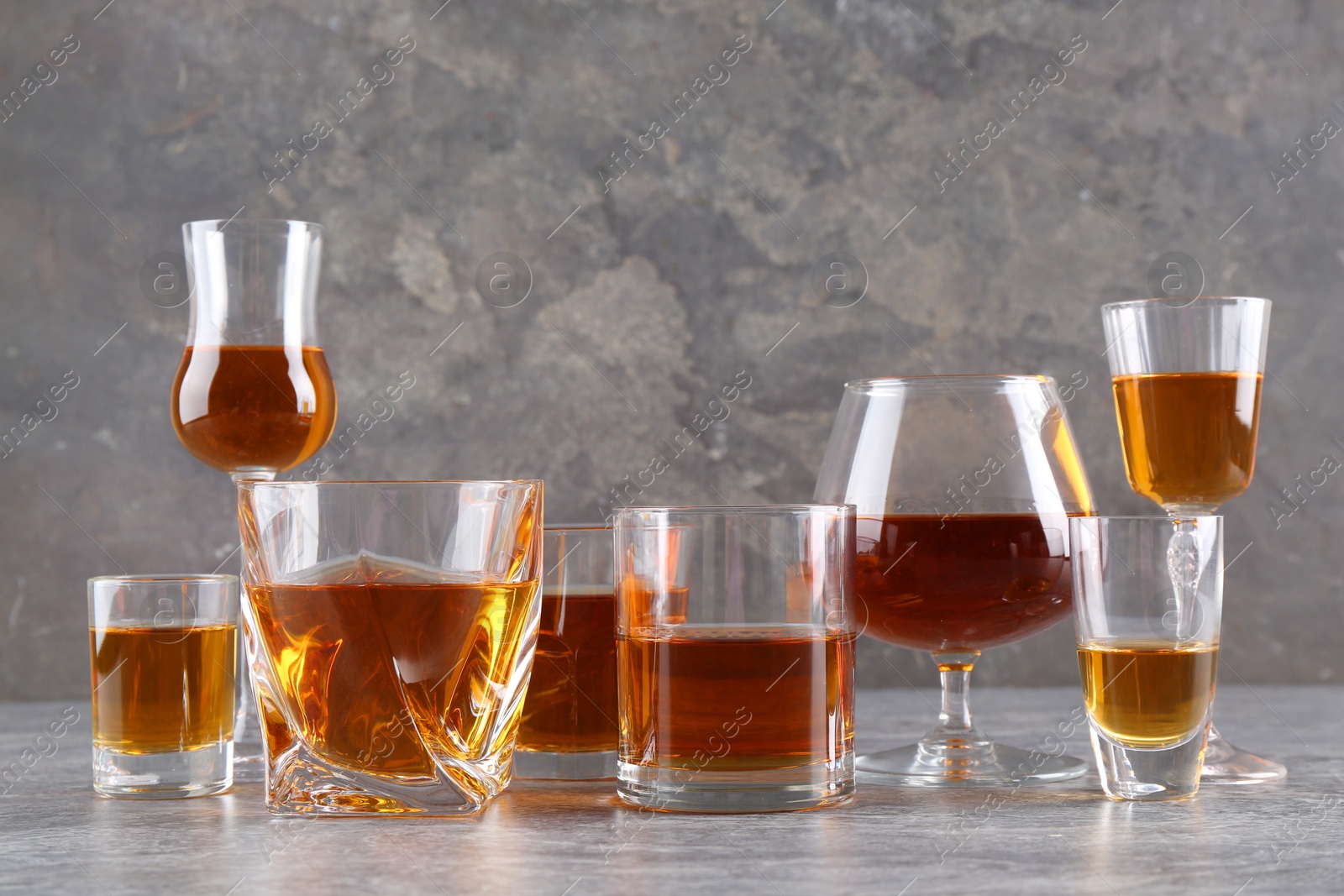 Photo of Many different liqueurs in glasses on grey textured table