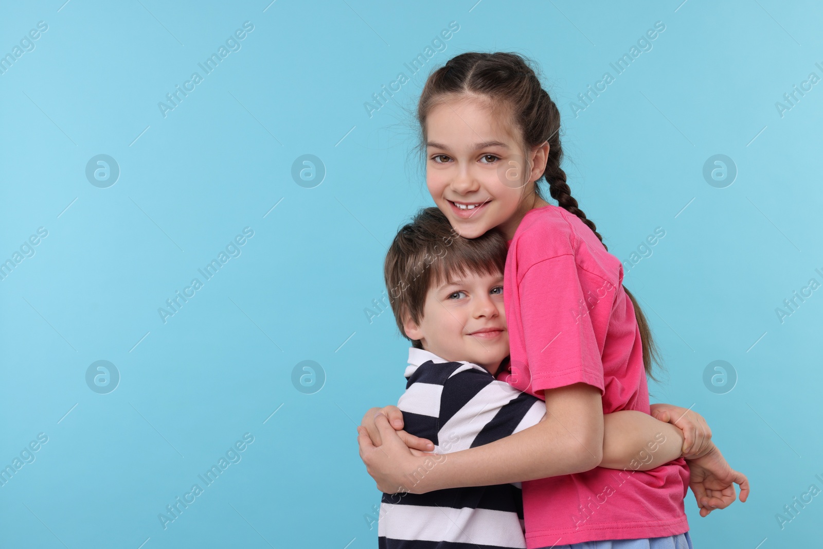 Photo of Happy brother and sister hugging on light blue background, space for text