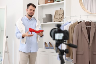 Photo of Smiling fashion blogger showing shoe while recording video at home