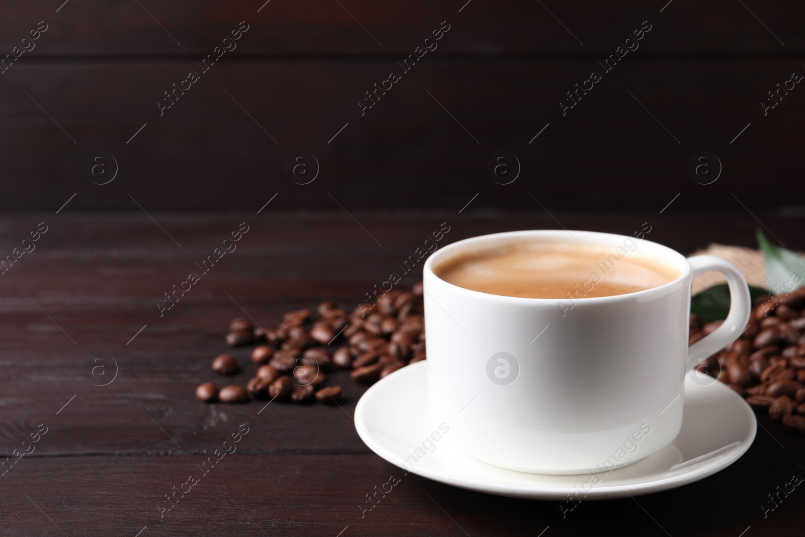 Photo of Cup of hot aromatic coffee and roasted beans on wooden table. Space for text