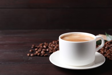 Cup of hot aromatic coffee and roasted beans on wooden table. Space for text