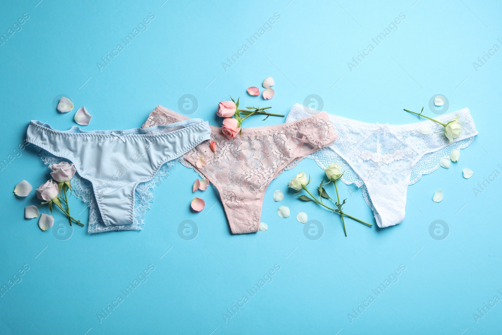 Photo of Set of elegant women's underwear and flowers on light blue background, flat lay