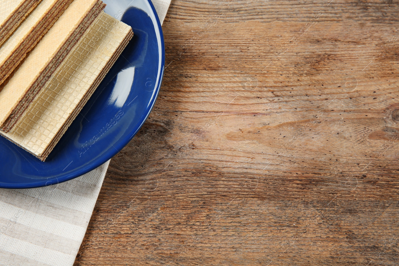 Photo of Plate of delicious wafers on brown wooden background, top view. Space for text