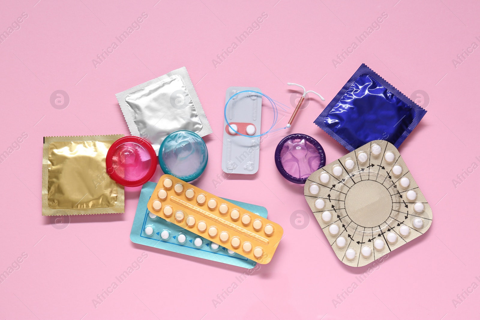 Photo of Contraceptive pills, condoms and intrauterine device on pink background, flat lay. Different birth control methods