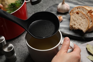 Woman pouring hot delicious bouillon into cup at grey table, closeup