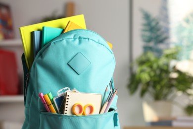 Turquoise backpack with different school stationery indoors, closeup. Space for text
