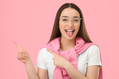Photo of Happy woman showing her tongue and pointing at something on pink background