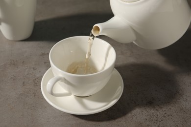 Photo of Pouring aromatic tea in cup at gray table, closeup