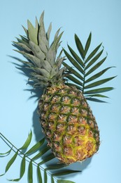 Photo of Whole ripe pineapple and green leaves on light blue background, flat lay