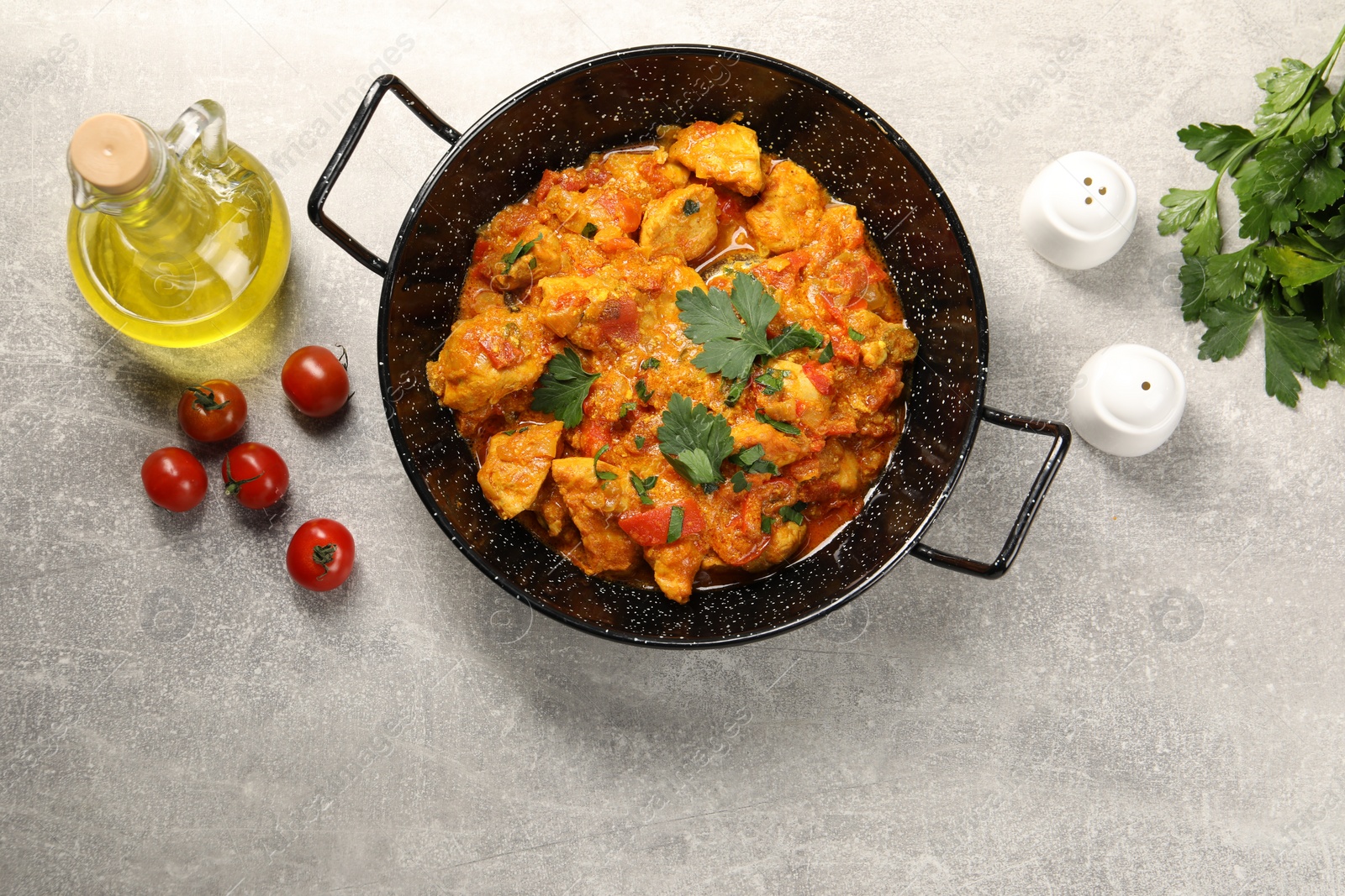 Photo of Delicious chicken curry in frying pan, parsley, tomatoes and oil on light grey table, flat lay