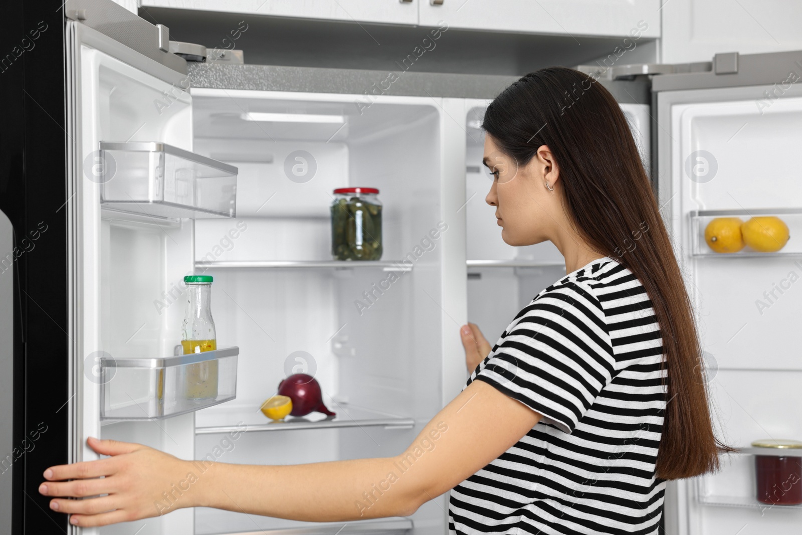 Photo of Upset woman near empty refrigerator in kitchen