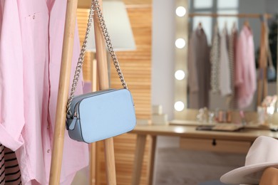 Photo of Clothes rack with light blue bag and pink shirt in makeup room, closeup