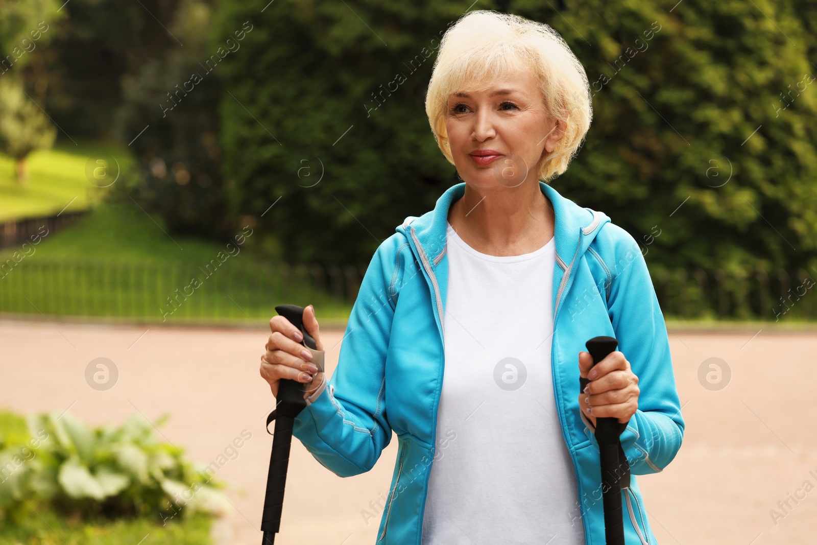 Photo of Senior woman with Nordic walking poles outdoors, space for text