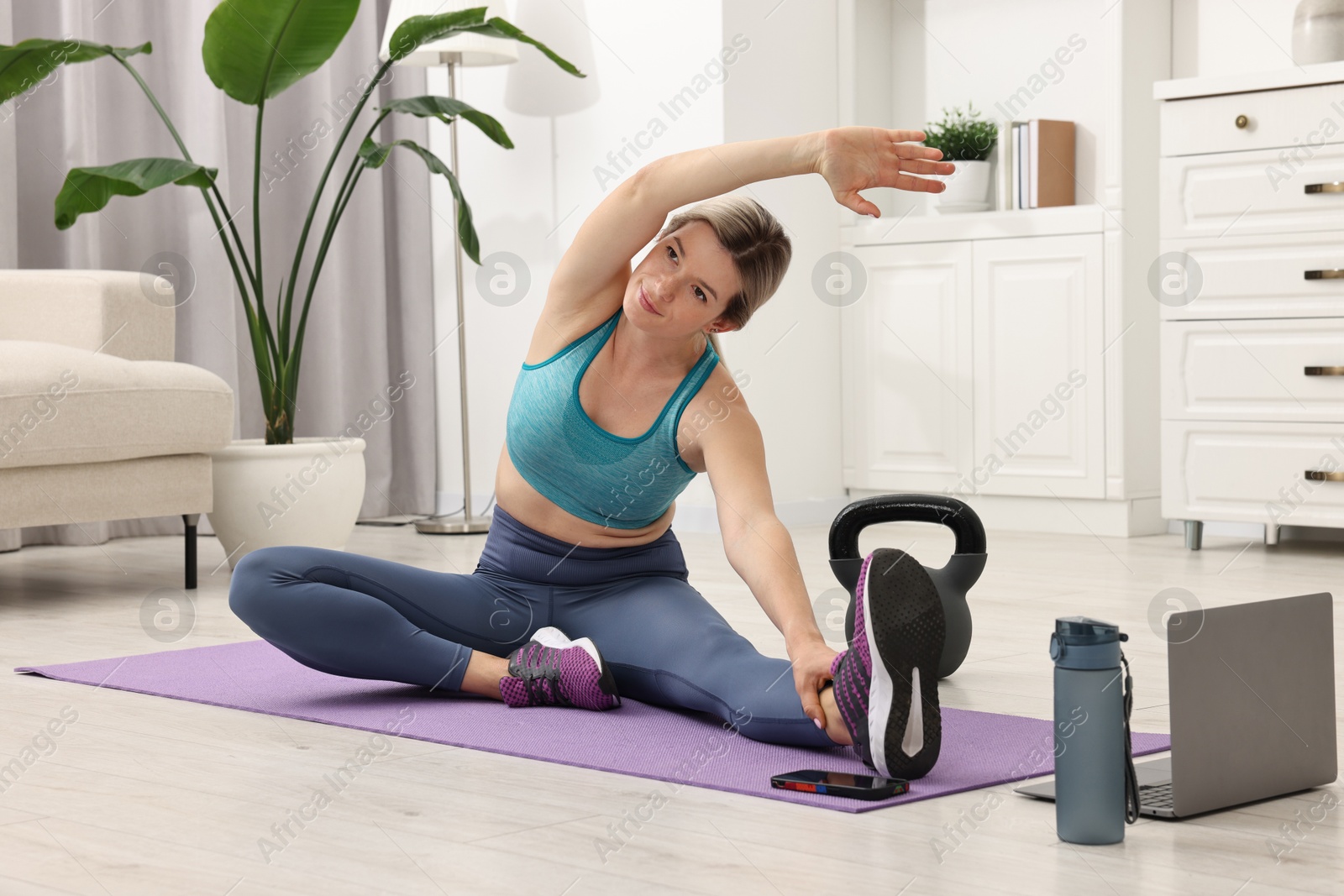 Photo of Online fitness trainer. Woman doing exercise near laptop at home