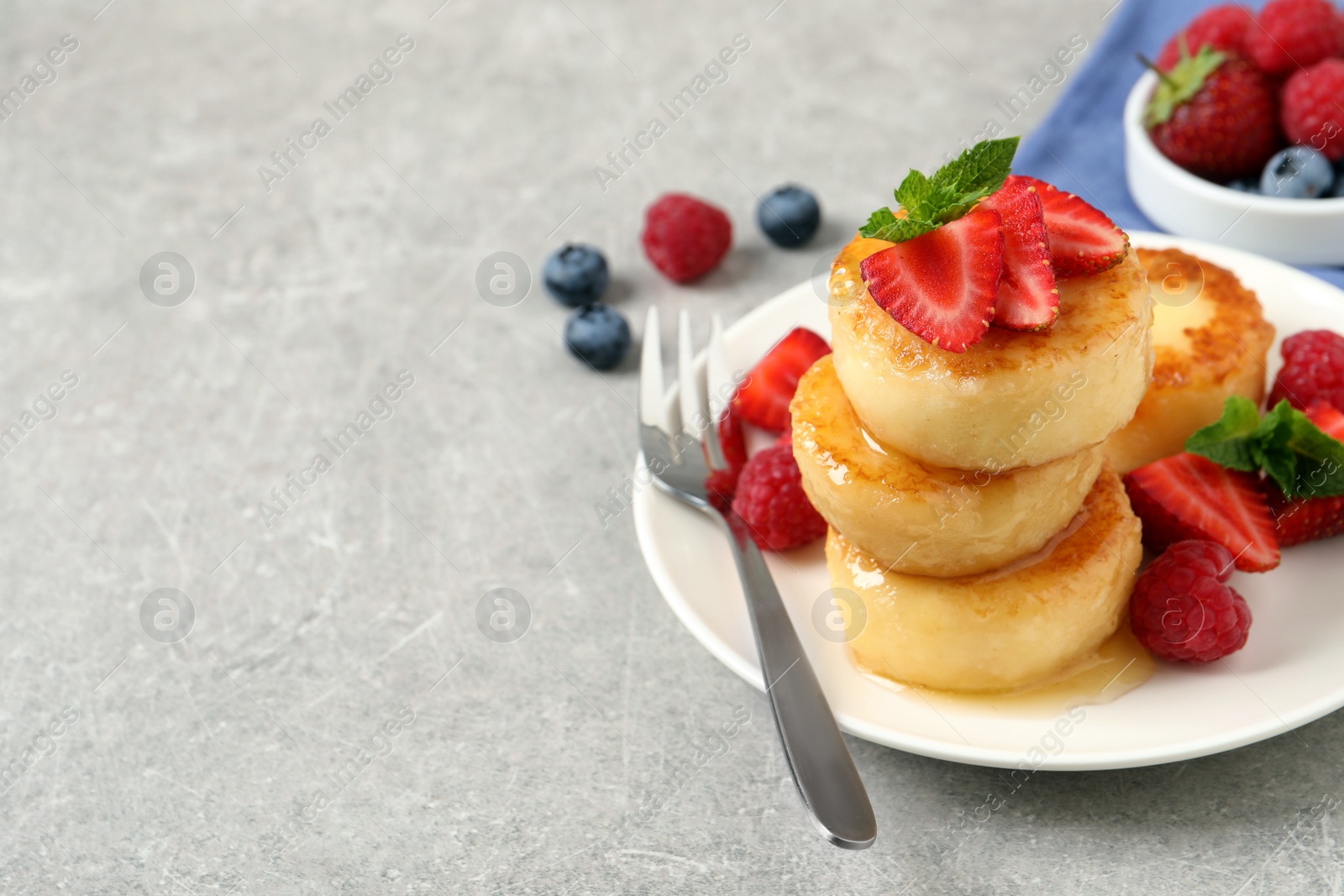 Photo of Delicious cottage cheese pancakes with fresh berries, mint and honey on light grey table, closeup. Space for text