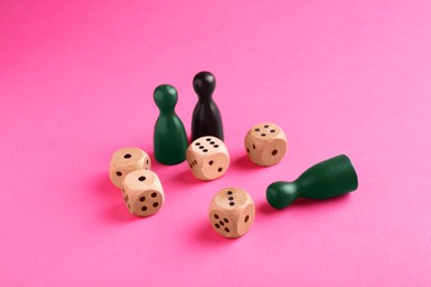 Wooden dices and color game pieces on pink background