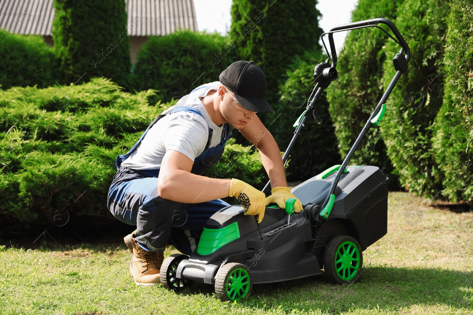 Photo of Young man with screwdriver fixing lawn mower in garden on sunny day