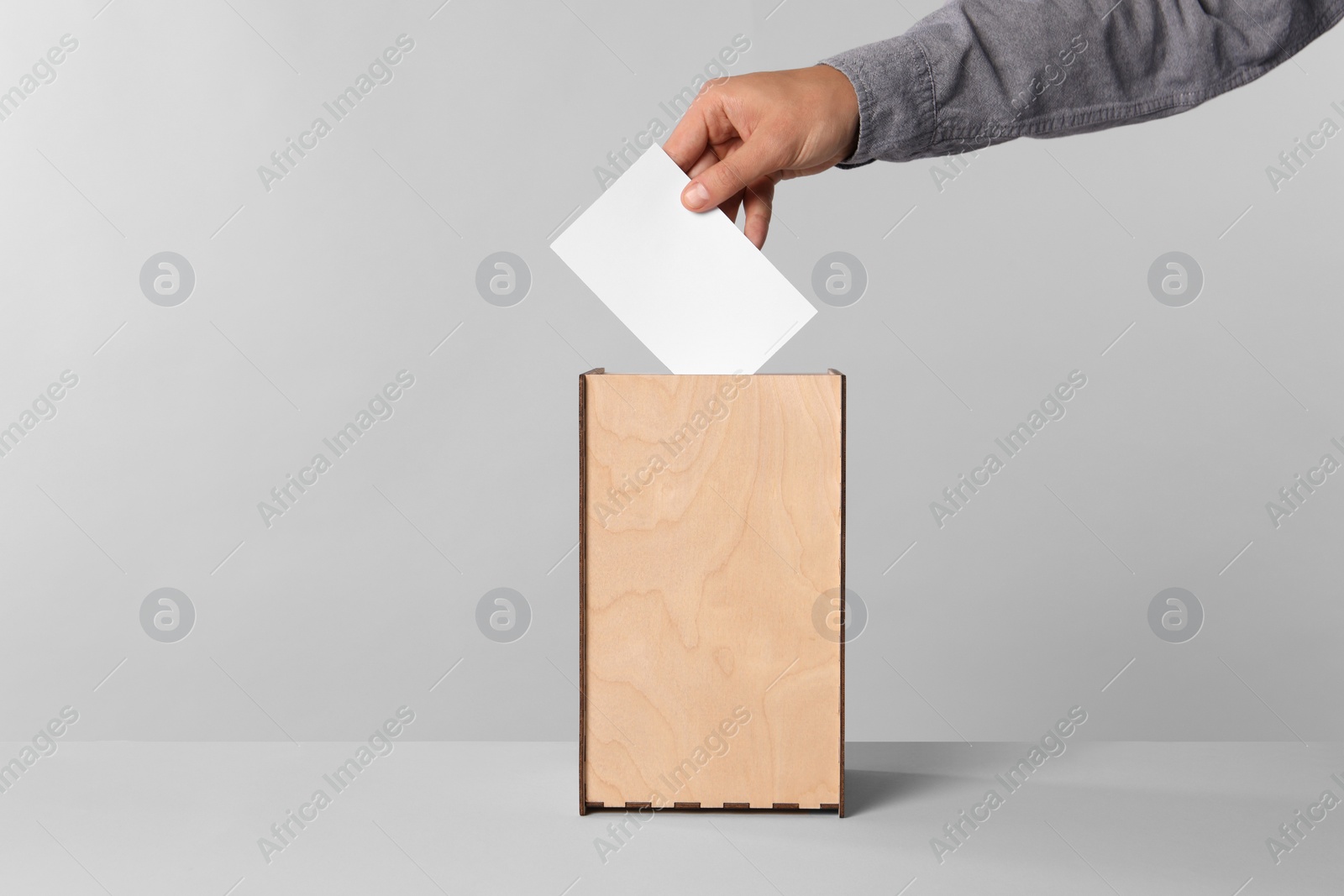 Photo of Man putting his vote into ballot box on light grey background, closeup