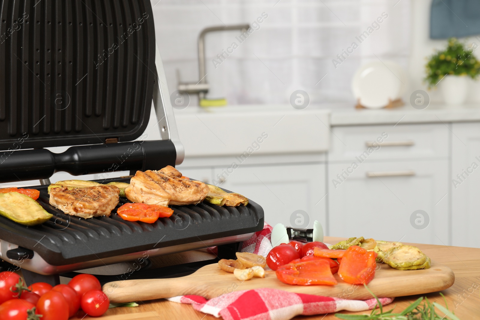 Photo of Electric grill, cooked meat and different products on wooden table