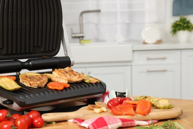 Photo of Electric grill, cooked meat and different products on wooden table