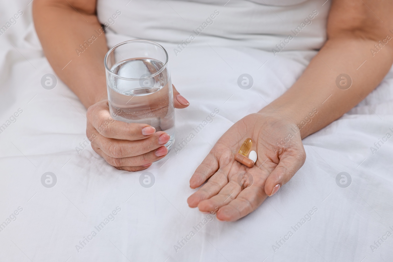 Photo of Woman with vitamin pills and glass of water in bed, closeup