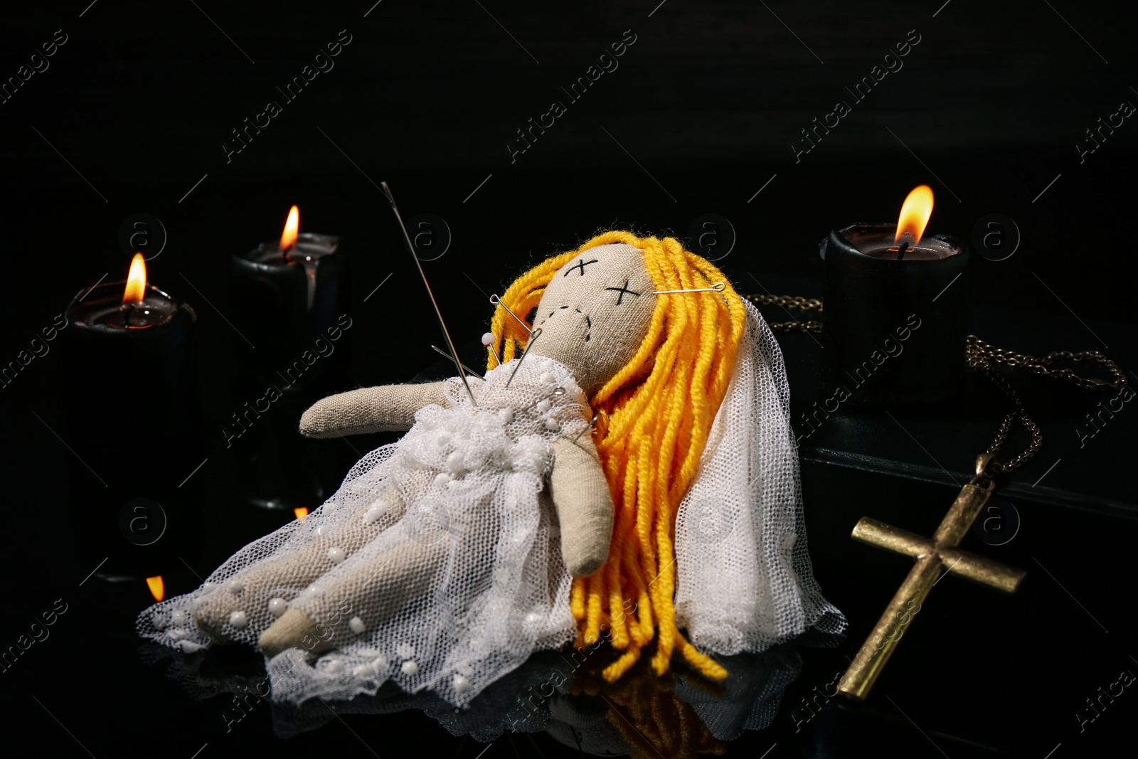 Photo of Voodoo doll pierced with pins, cross and candles on black table. Curse ceremony