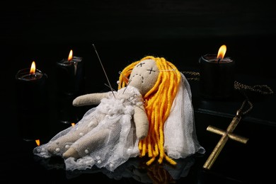 Photo of Voodoo doll pierced with pins, cross and candles on black table. Curse ceremony