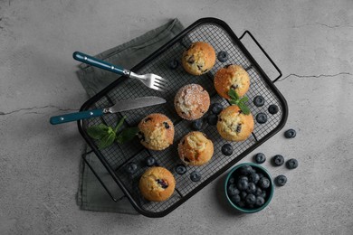 Photo of Delicious muffins with powdered sugar, blueberries and cutlery on light grey table, flat lay
