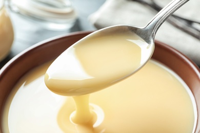 Spoon of pouring condensed milk over bowl, closeup. Dairy products