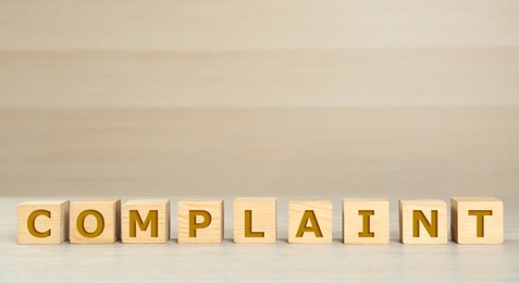 Image of Word Complaint made of cubes on light wooden table. Space for text