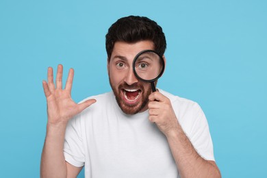 Photo of Emotional man looking through magnifier glass on light blue background