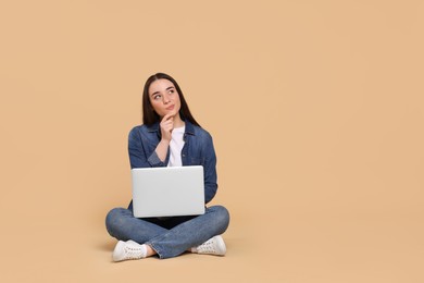 Photo of Thoughtful young woman with laptop on beige background, space for text
