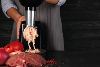 Photo of Woman making chicken mince with electric meat grinder at black table, closeup. Space for text