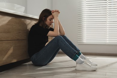 Photo of Sad young woman sitting on floor indoors