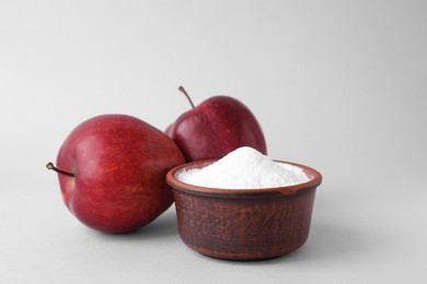 Bowl with sweet fructose powder and ripe apples on white background