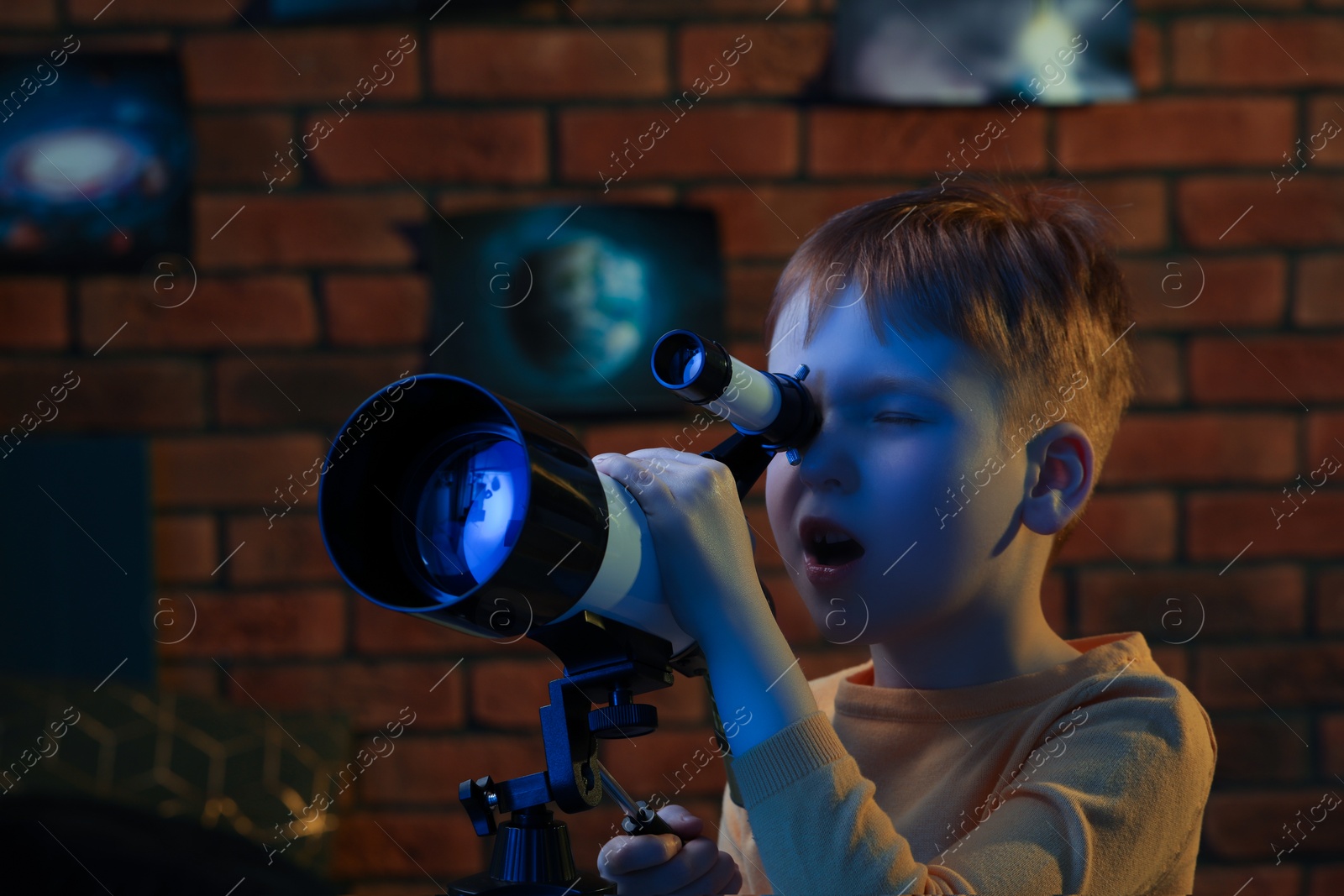 Photo of Little boy looking at stars through telescope in room