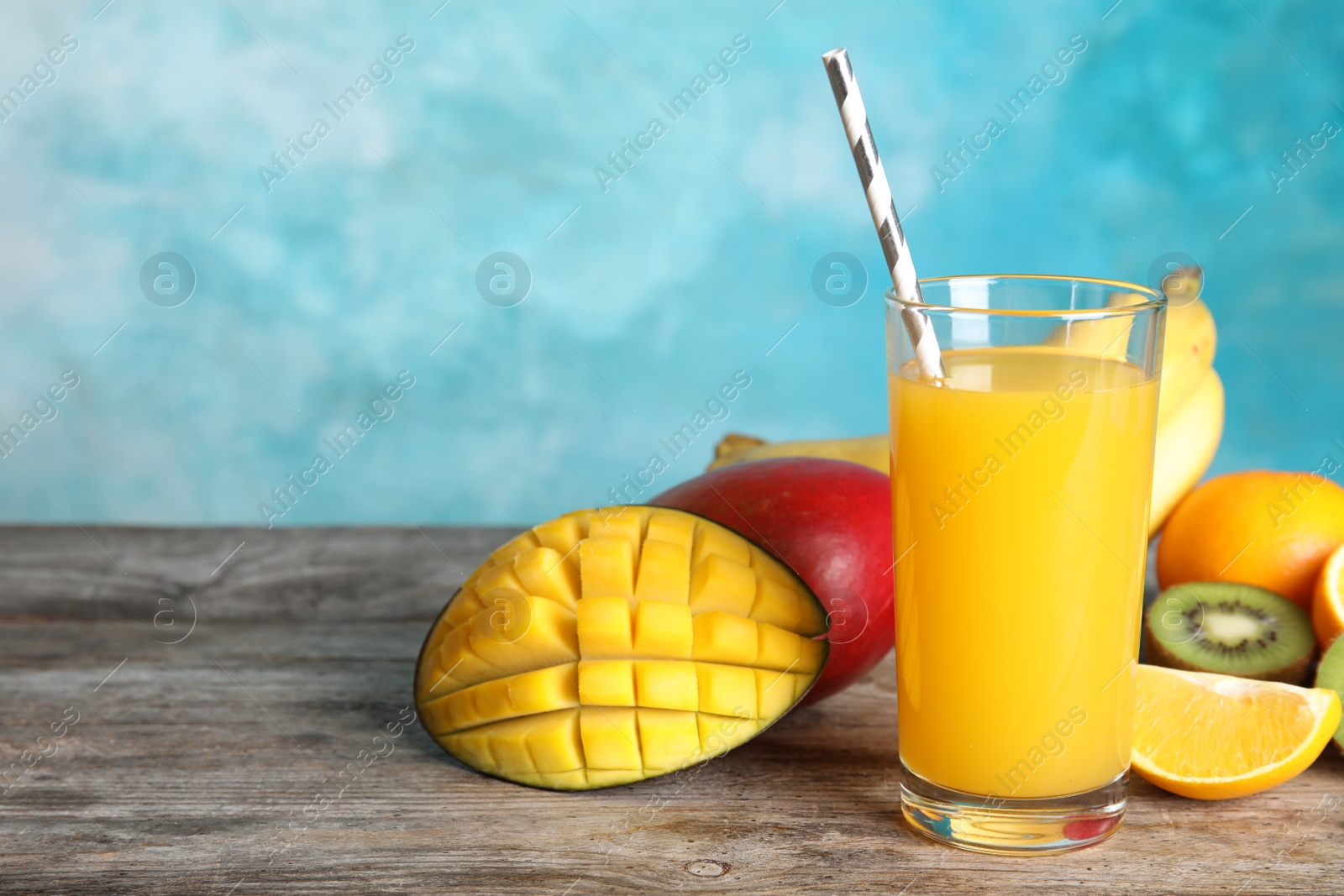 Photo of Glass with tasty mango juice and fresh fruits on table against color background. Space for text