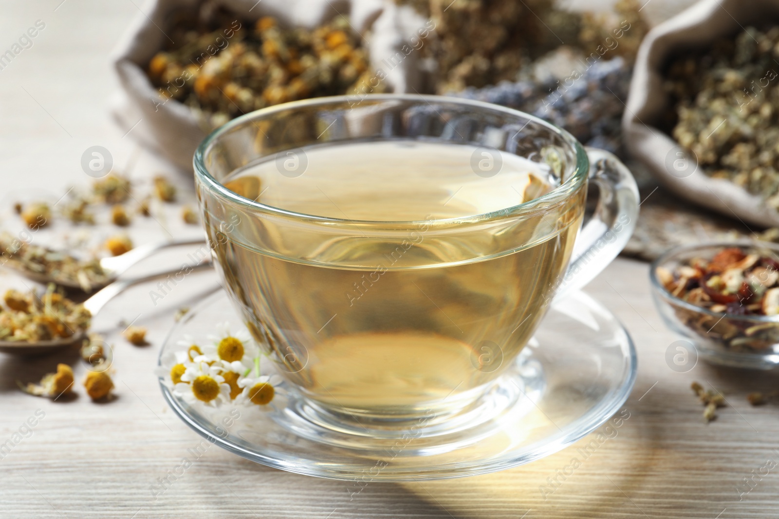 Photo of Glass cup of aromatic freshly brewed tea near different dry herbs on wooden table