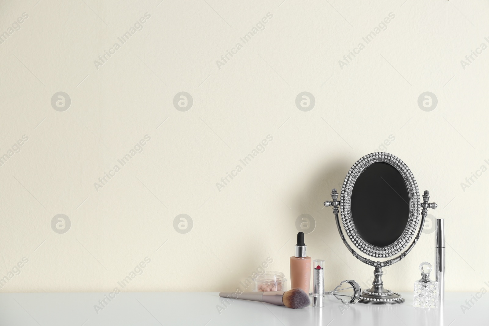 Photo of Mirror and makeup products on white table near light wall. Space for text