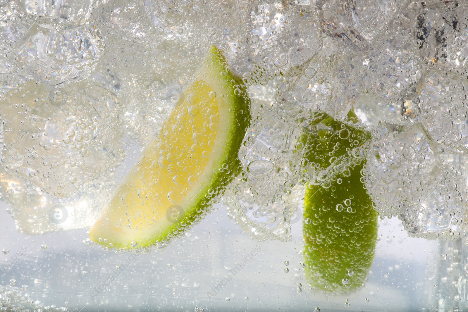 Photo of Juicy lime slices and ice cubes in soda water against white background, closeup