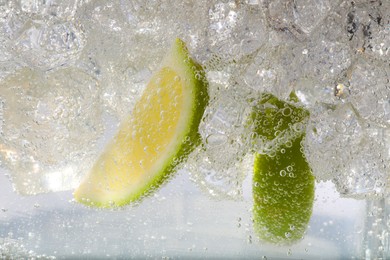 Photo of Juicy lime slices and ice cubes in soda water against white background, closeup