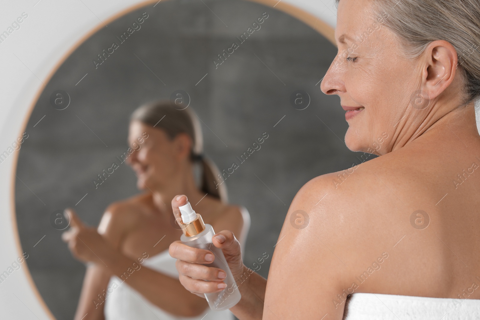 Photo of Happy woman applying body oil onto shoulder near mirror indoors. Space for text