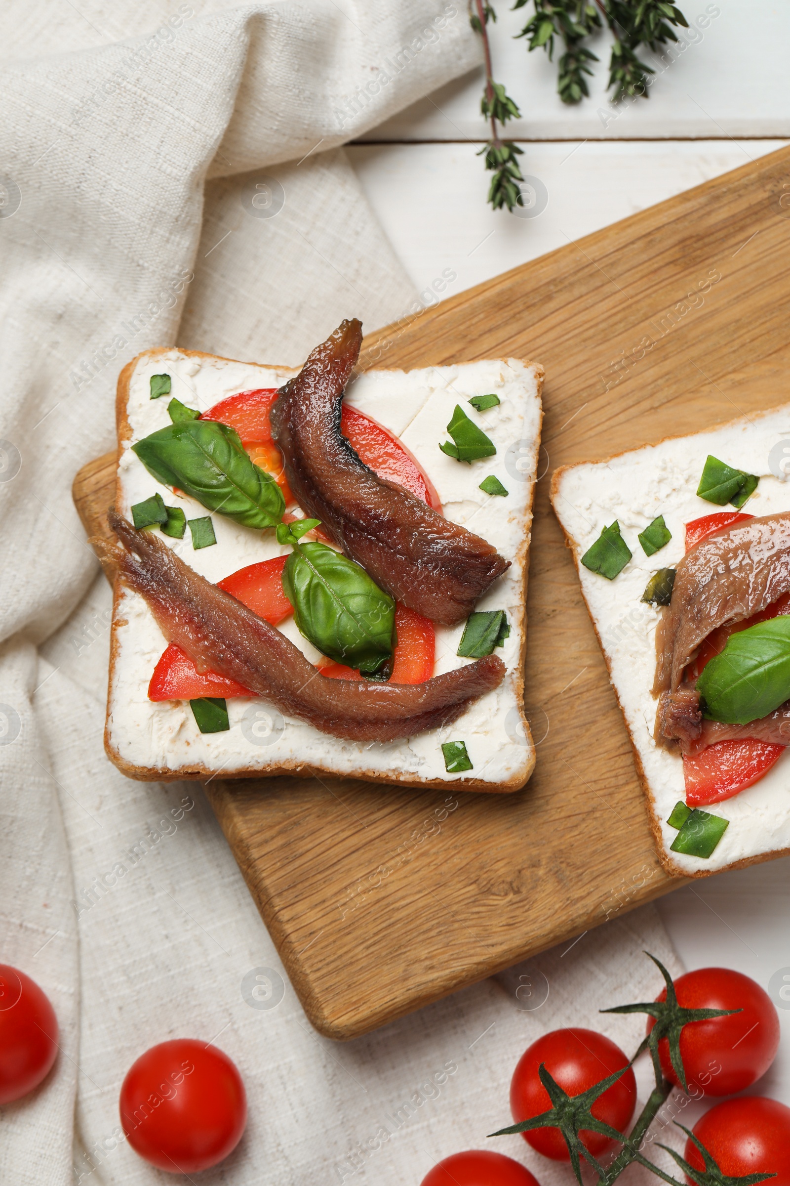 Photo of Delicious sandwiches with cream cheese, anchovies, tomatoes and basil on white wooden table, flat lay