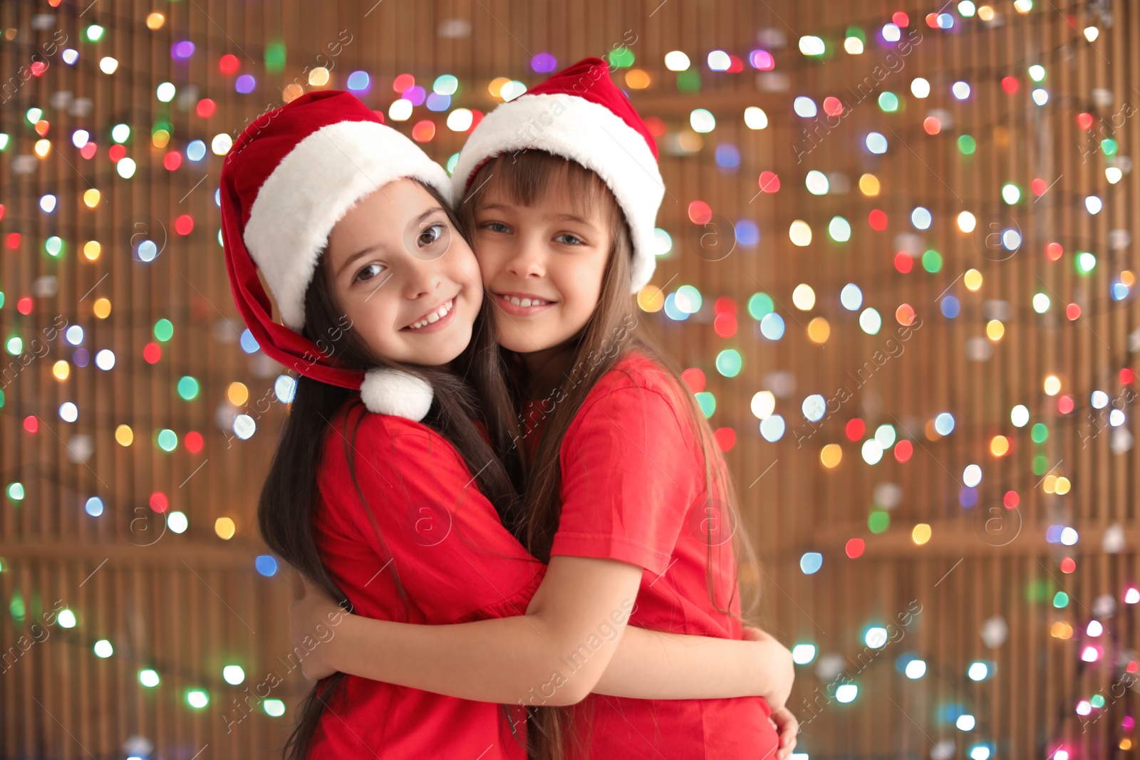 Photo of Cute little children in Santa hats on blurred lights background. Christmas celebration