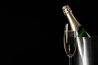 Glass of champagne near bucket with bottle on black background, space for text