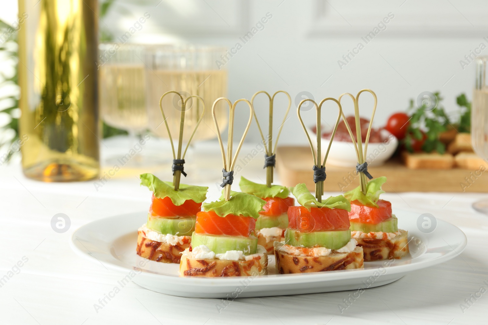 Photo of Tasty canapes with salmon, cucumber, bread and cream cheese on white wooden table